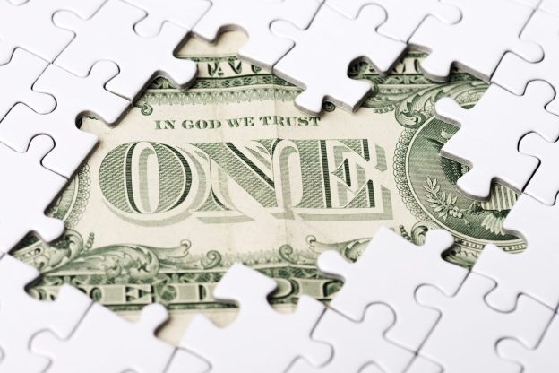 one dollar bill emerging under puzzle