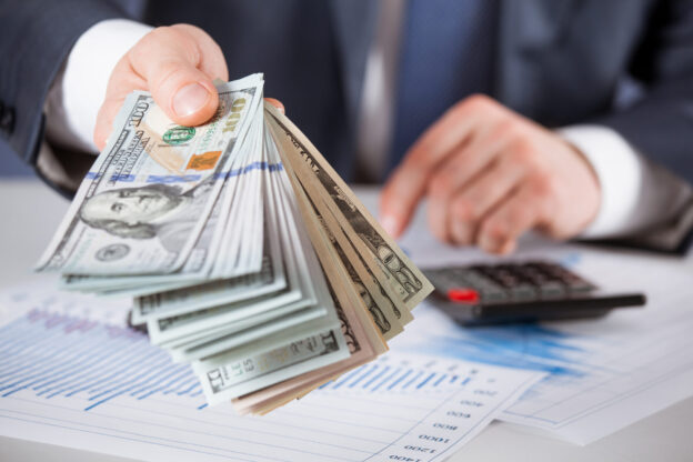 A man in a business suit holding out cash for payroll