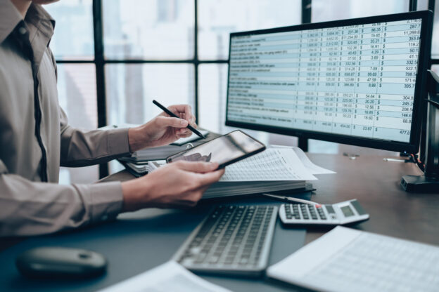 Investor working on desk office and using tablet to check tracking cost spreadsheet.
